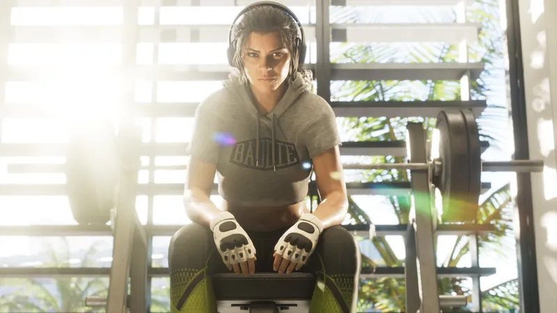 Lucia in a crop hoodie and lifting gloves sitting on a bench press in a sunlit gym