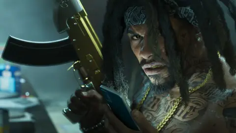 A man with dreadlocks and a gold-plated rifle checking his phone in a dim room